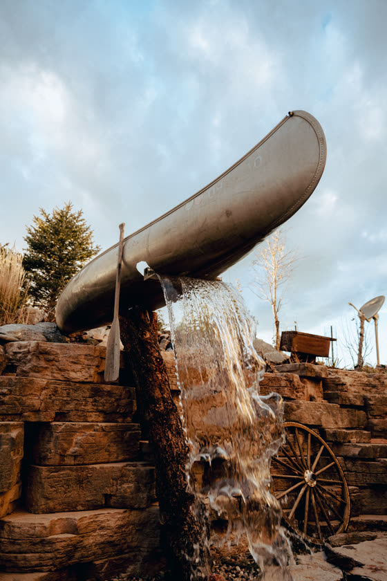 Canoe water feature pouring over a stacked stone waterfall
