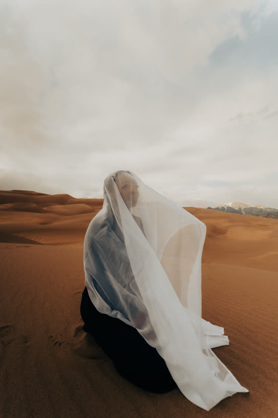 Figure draped in white fabric on a windswept dune