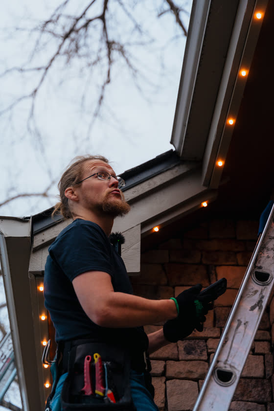 Installer on a ladder running string lights along a patio